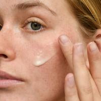 A woman applying a smear of Farmacy's Filling Good Mini Hyaluronic Acid Plumping Serum to her cheek
